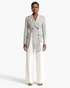 Beach Rose Co. light gray asymmetrical double-breasted blazer with notched lapels worn with white wide-leg trousers.