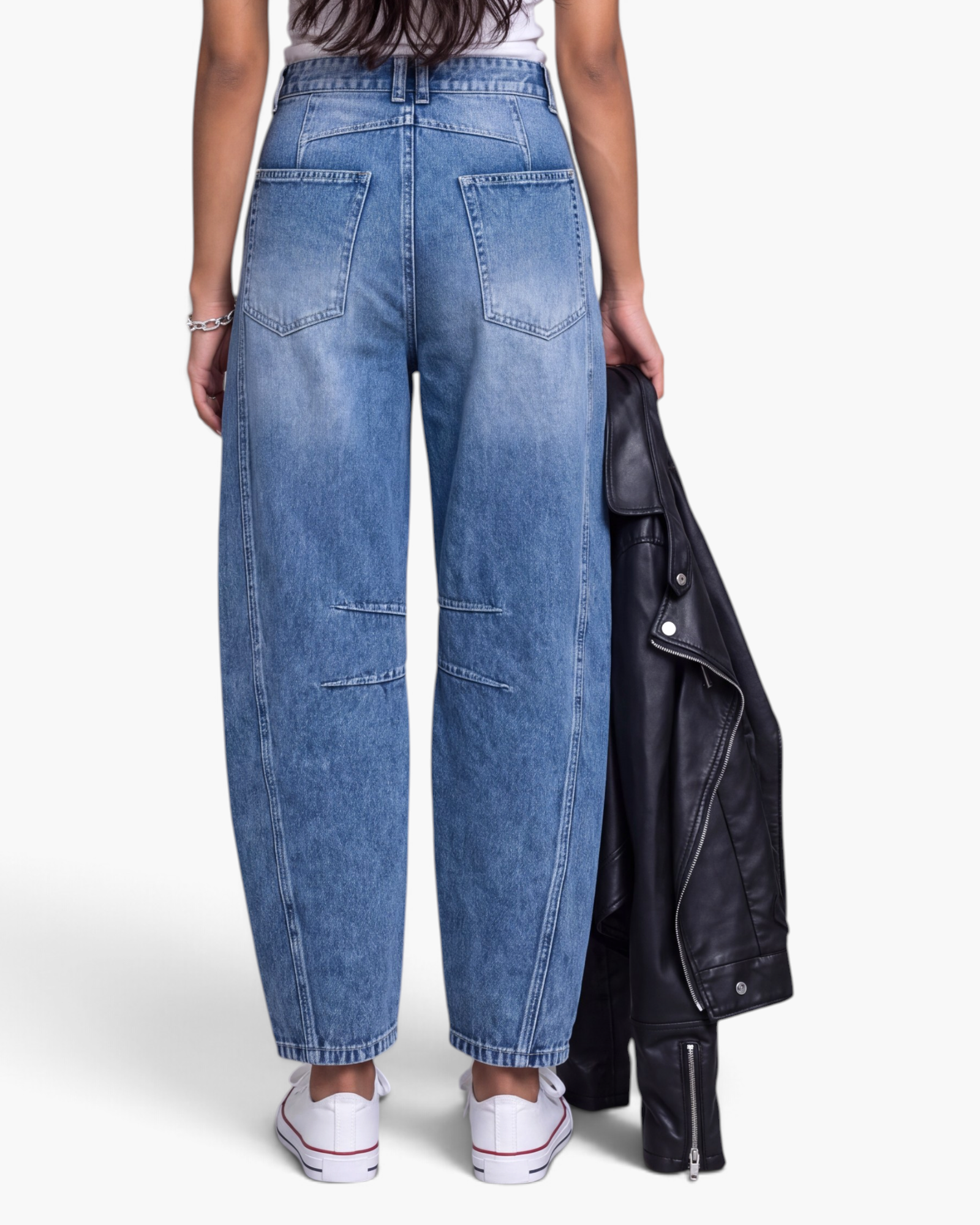 Beach Rose Co. blue barrel leg jeans with knee darts and curved seams, worn by a model holding a black leather jacket.