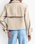 Beach Rose Co. beige cropped trench jacket with back storm flap and buckled cuffs worn with light wash jeans