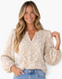 Beach Rose Co. beige blouse with cream floral texture, split neckline, and long balloon sleeves on a smiling model.
