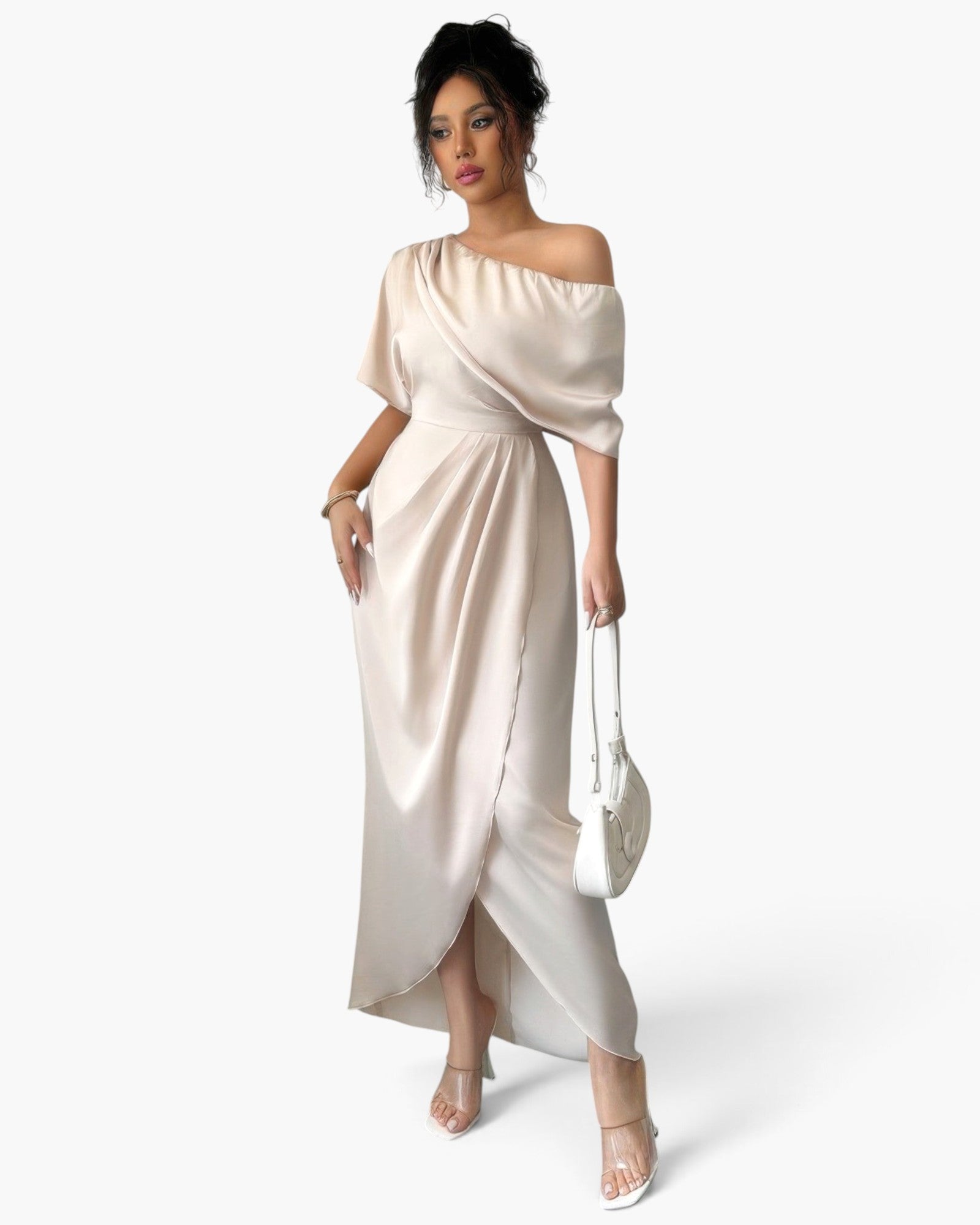 A woman shown from the back wearing a floor-length off-shoulder gown in a light warm beige or cream tone against a plain light gray studio background.