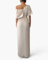 A woman shown from the back wearing a floor-length off-shoulder gown in a light warm beige or cream tone against a plain light gray studio background.