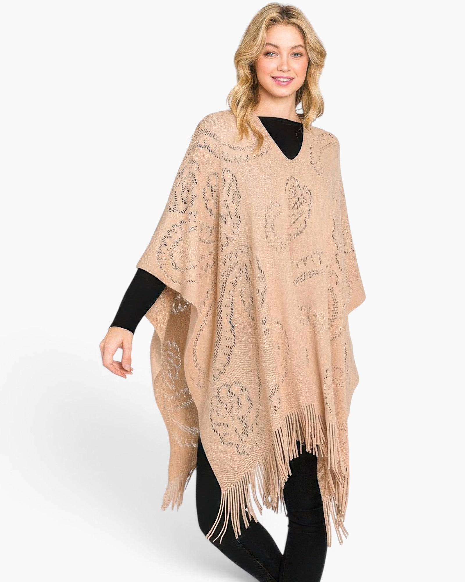 Beach Rose Co. beige acrylic poncho with paisley pattern and fringe hem worn by a blonde model over a black outfit.