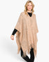 Beach Rose Co. beige acrylic poncho with paisley pattern and fringe hem worn by a blonde model over a black outfit.