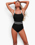 Beach Rose Co. black one-piece swimsuit with white trim and cross-back straps worn by a woman on a sunny beach.