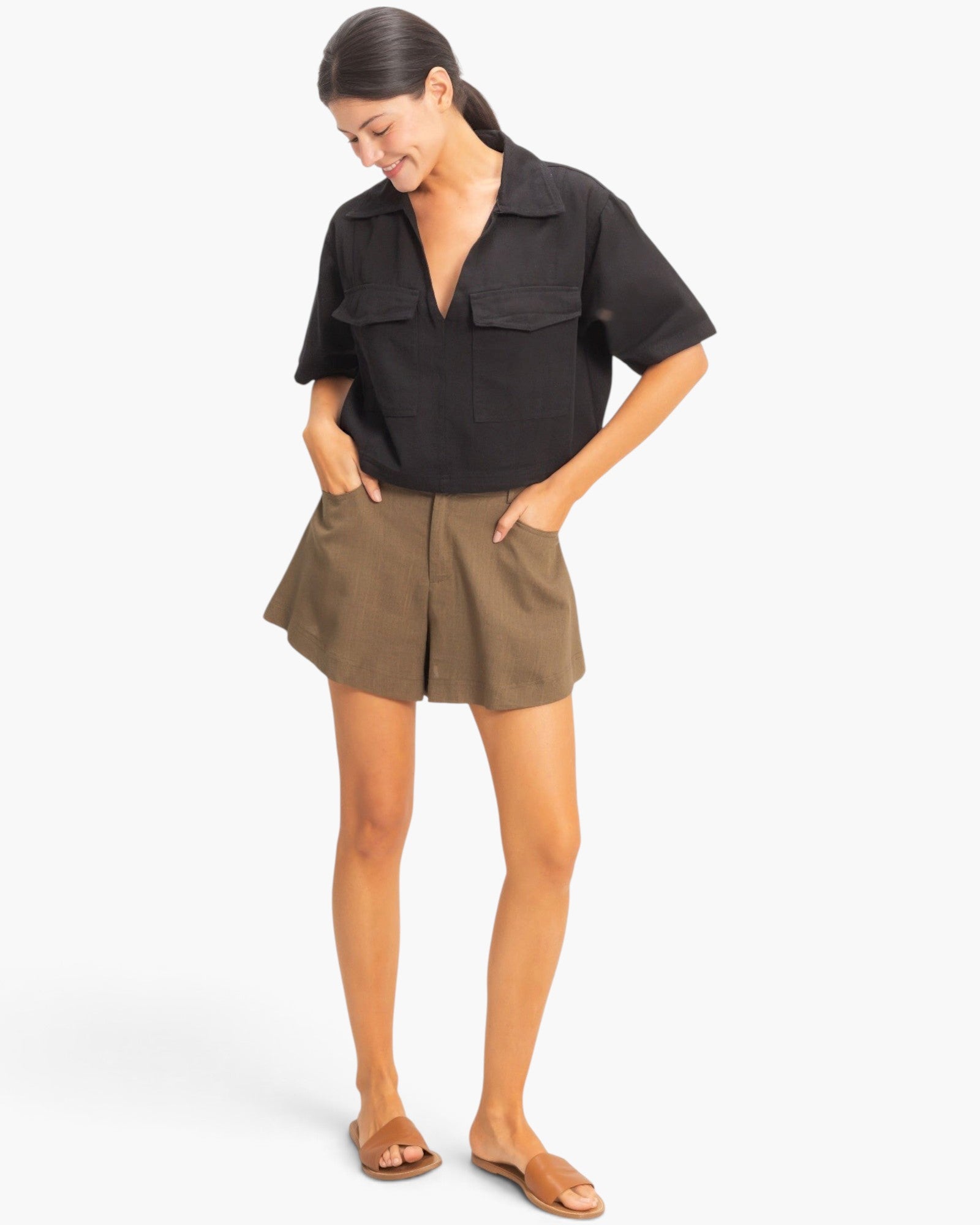 Beach Rose Co. black cotton collared V-neck top with short sleeves and front flap pockets worn with brown shorts.
