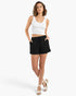 A woman wearing Beach Rose Co. black cotton comfort shorts with a white tank top, standing against a white background.