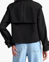 Beach Rose Co. black cropped trench jacket featuring a back storm flap and buckled cuffs, worn with light blue jeans.