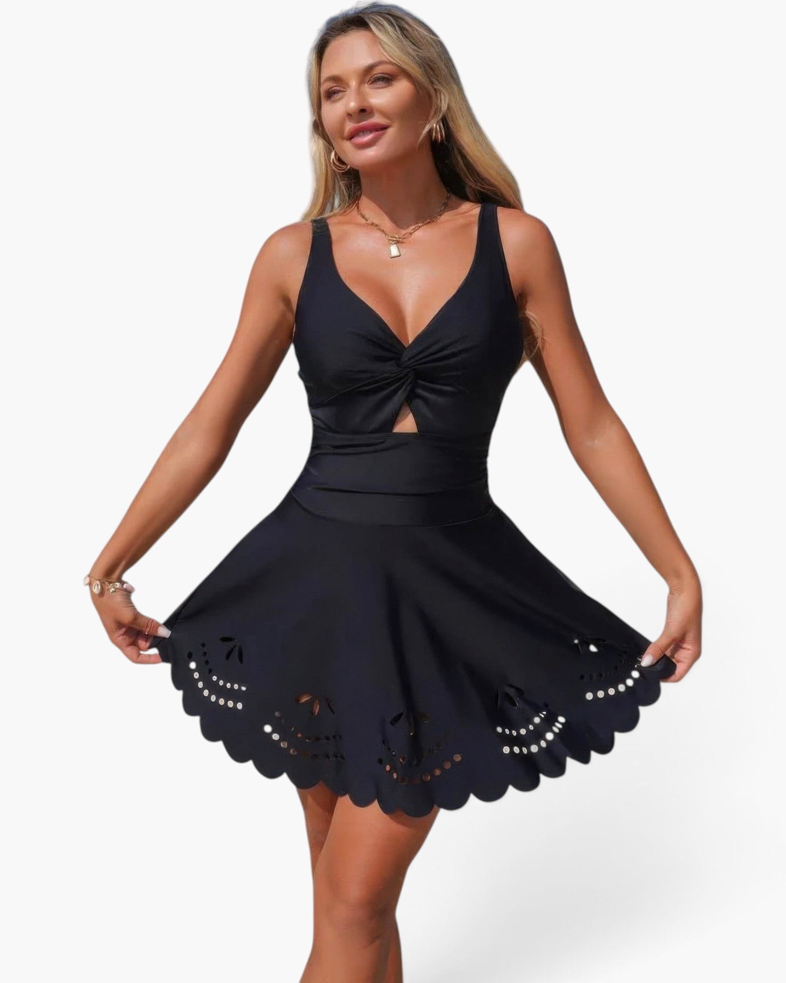 A woman modeling a black sleeveless mini dress with a deep V-neckline, twisted front detail, a fitted waist, and a flared skirt with scalloped eyelet lace trim, against a light gray studio background.
