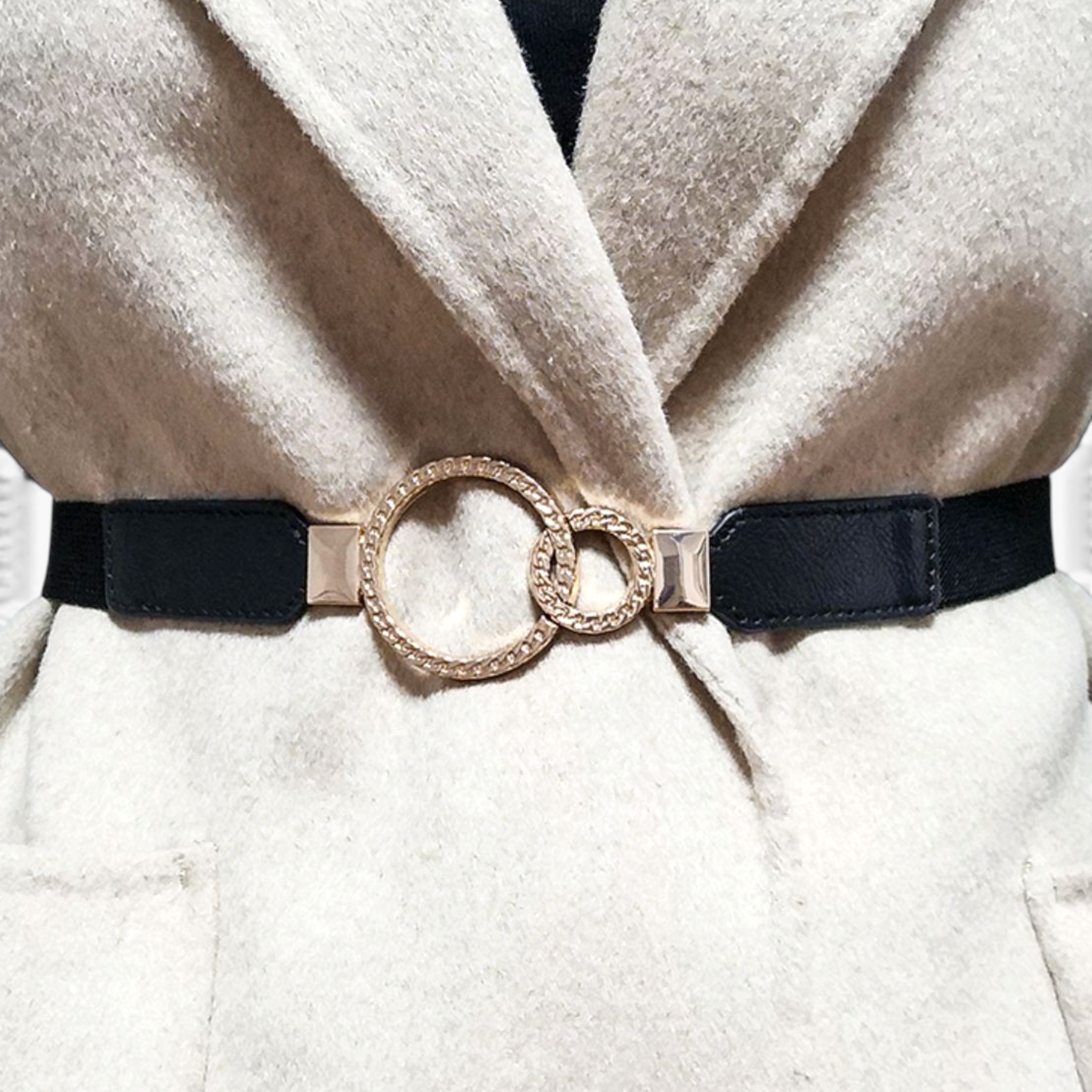 Beach Rose Co. slim black elastic waist belt featuring an asymmetric double-ring gold buckle worn over a beige coat.