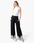 Beach Rose Co. black wide-leg pants with white embroidered hems, elastic waistband, and pockets on a model.