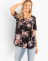 Beach Rose Co. black floral babydoll top with a crisscross V-neckline and short sleeves on a smiling model