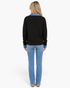Back view of a blonde woman wearing a Beach Rose Co. black knit sweater with a denim collar and cuffs over blue jeans.