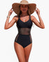 Beach Rose Co. black one-piece swimsuit with mesh panels, ring-accented straps, and a wide-brimmed straw sun hat.