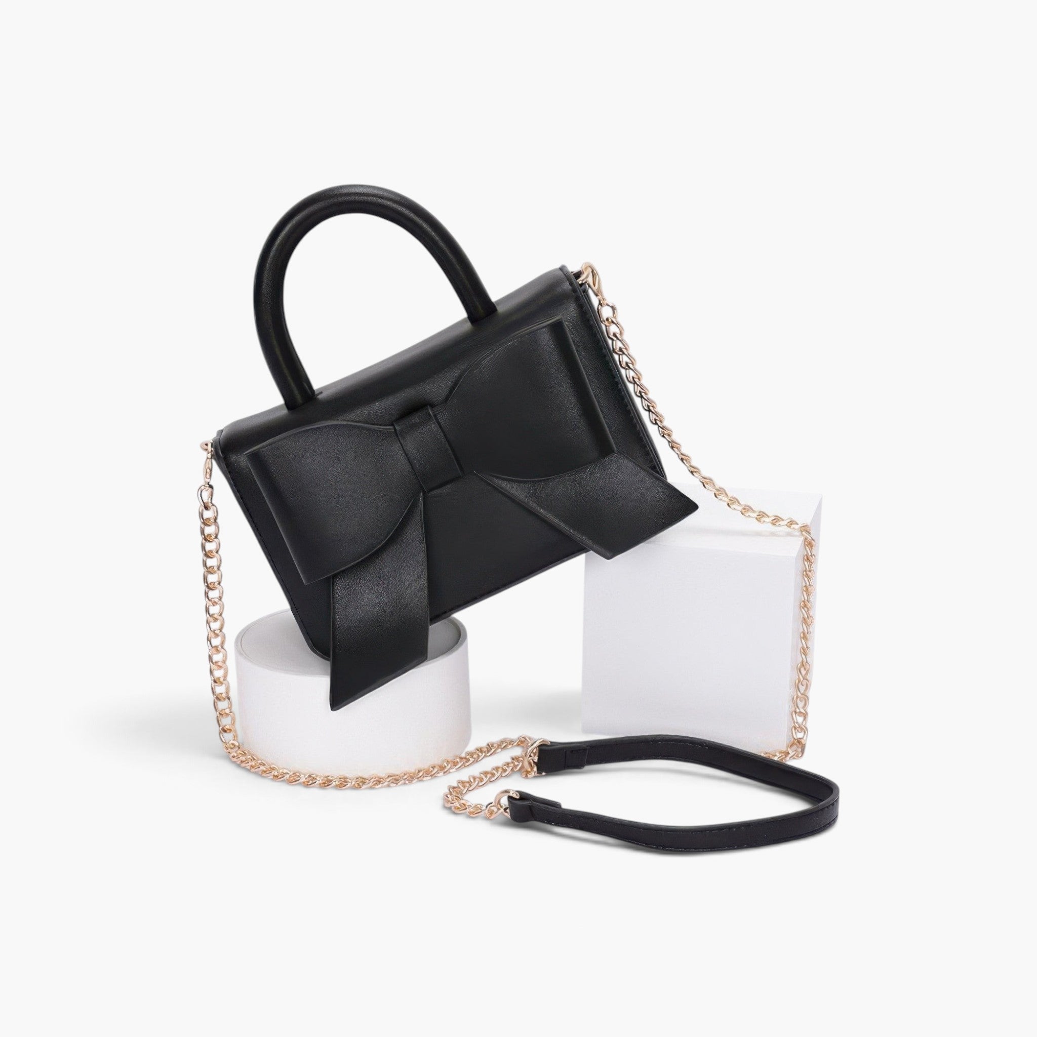 Beach Rose Co. black faux leather handbag featuring a decorative ribbon bow, top handle, and gold chain shoulder strap.
