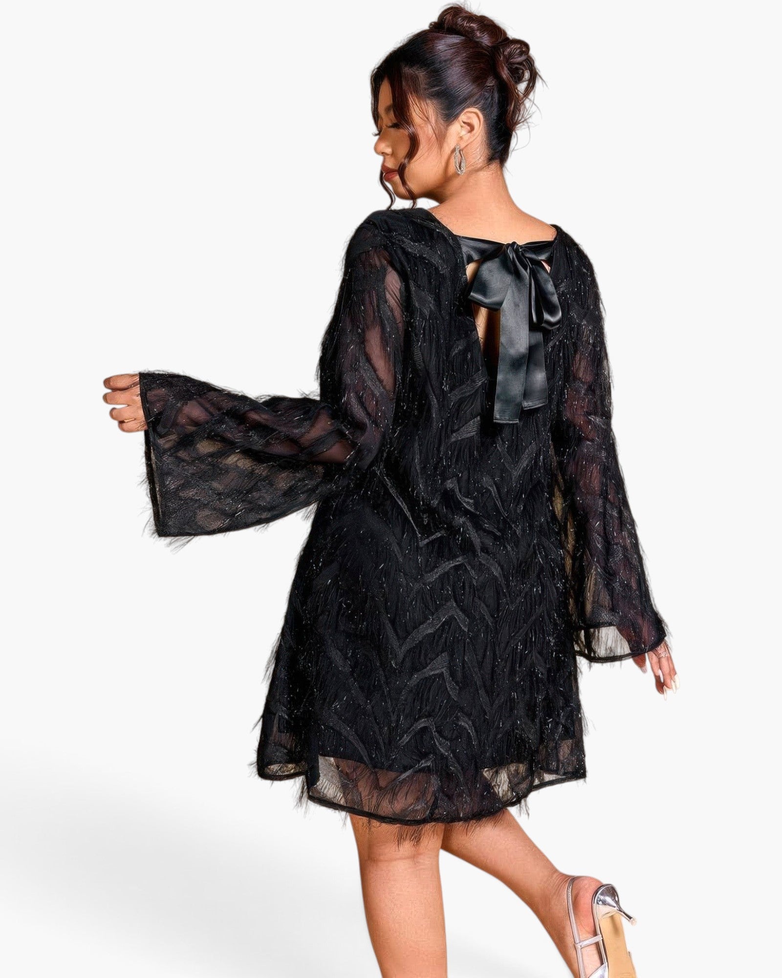 A woman modeling a black sheer lace long-sleeve dress from the back, featuring a large bow at the neckline and a textured chevron pattern, set against a plain white background.