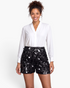 Model wearing Beach Rose Co. black sequin shorts with mixed-size discs and a white long-sleeve blouse.
