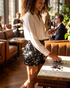 Beach Rose Co. black sequin shorts with mixed-size discs worn with a white blouse in a restaurant setting.