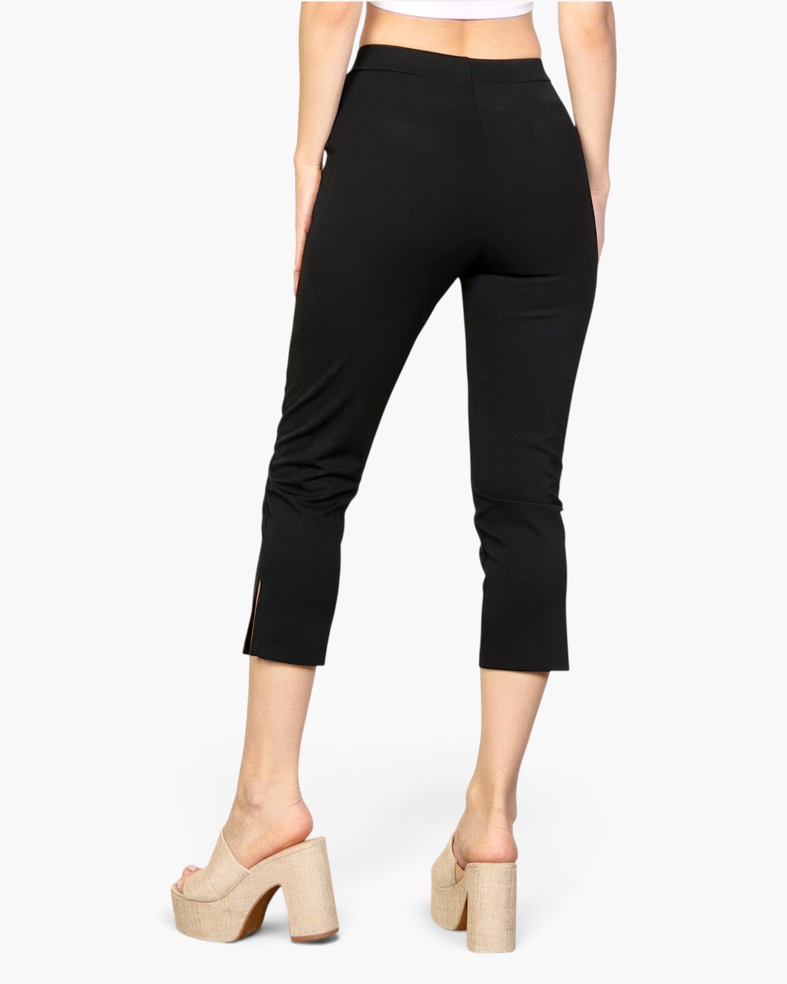Beach Rose Co. black cropped pants with a slit hem detail, worn by a model in beige platform mules, back view.