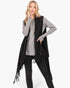 Beach Rose Co. black knit vest with embossed dotted lines and tassel fringe worn by a blonde model over a grey top.