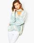 Beach Rose Co. blue surf tie-dye surplice top with a trendy choker neckline worn by a model with white jeans.