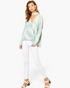 Beach Rose Co. blue surf tie-dye surplice top with a choker neckline worn by a model with white jeans and heels.
