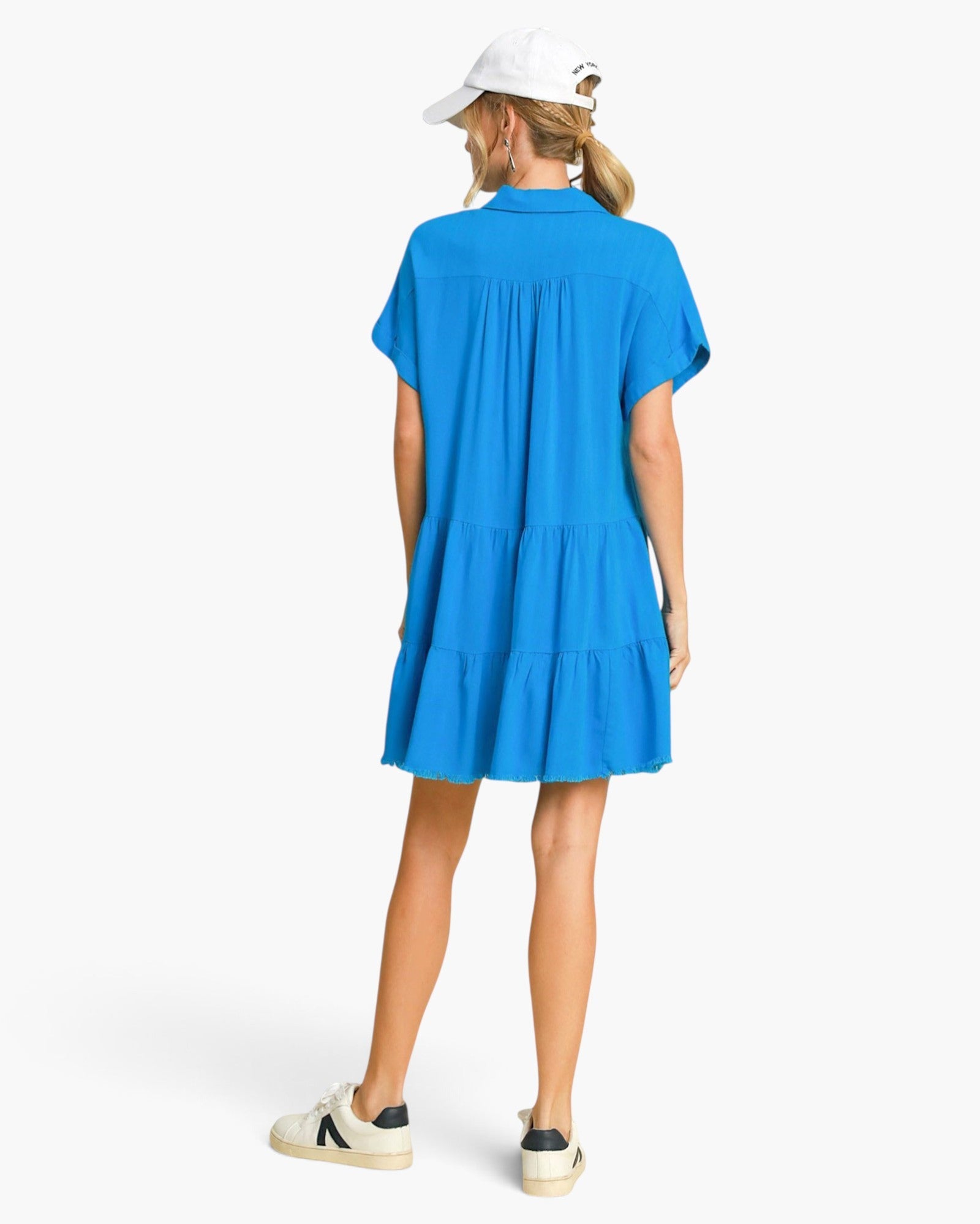 Back view of a woman wearing a Beach Rose Co. ocean blue linen-blend tiered mini dress with a frayed hem and collar.