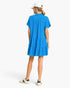 Back view of a woman wearing a Beach Rose Co. ocean blue linen-blend tiered mini dress with a frayed hem and collar.