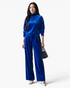 Beach Rose Co. blue velvet mock neck top and wide leg pants set worn by a model with a black handbag.