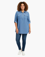 Beach Rose Co. blue zip-front tunic blouse with utility pockets and roll-tab sleeves worn by a curly-haired model.