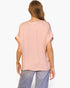 Back view of a model wearing a Beach Rose Co. blush pink washed poly silk V-neck tee with cuffed short sleeves.