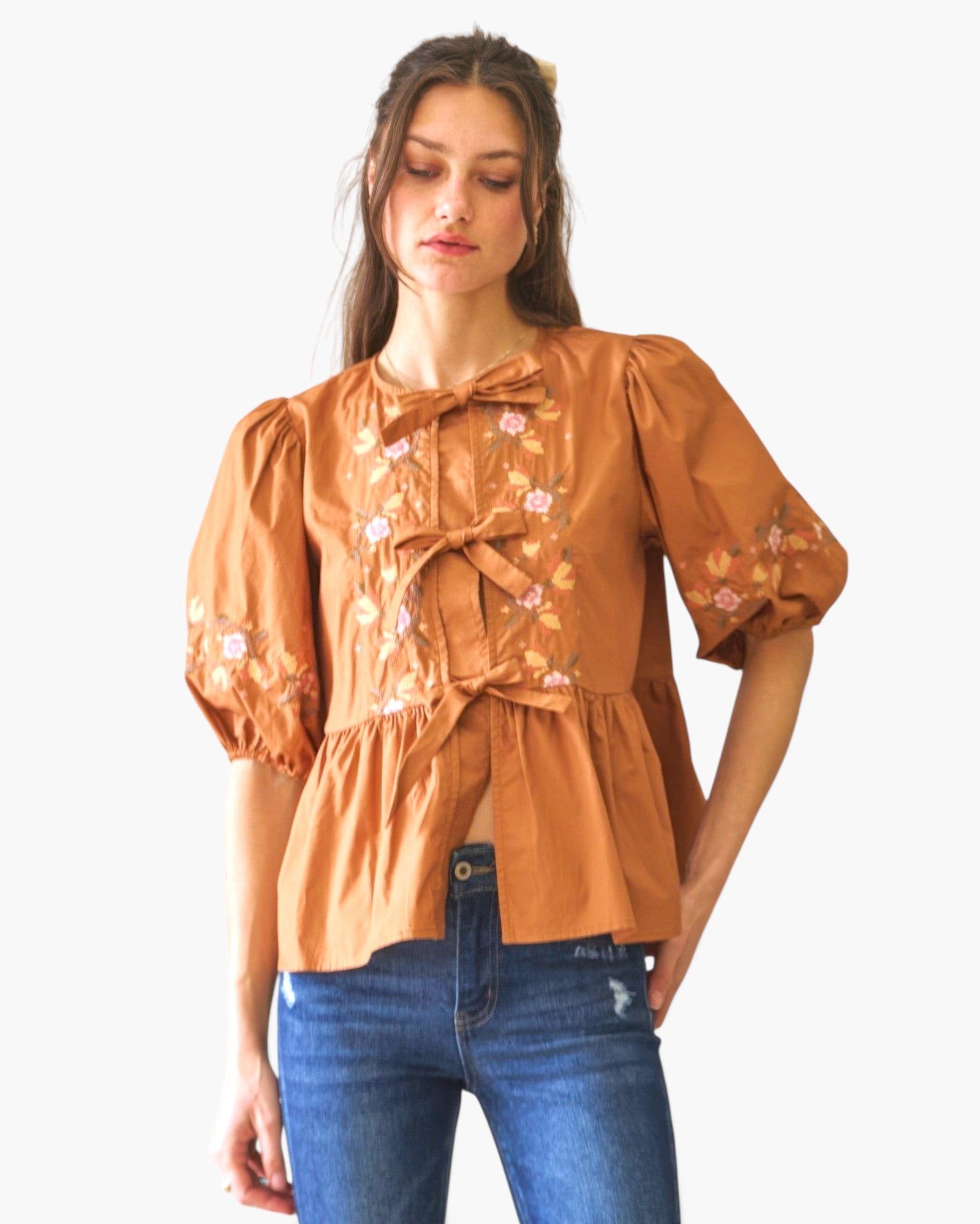 Beach Rose Co. brown poplin blouse with front ribbon ties, floral embroidery, and puff sleeves worn with blue jeans.
