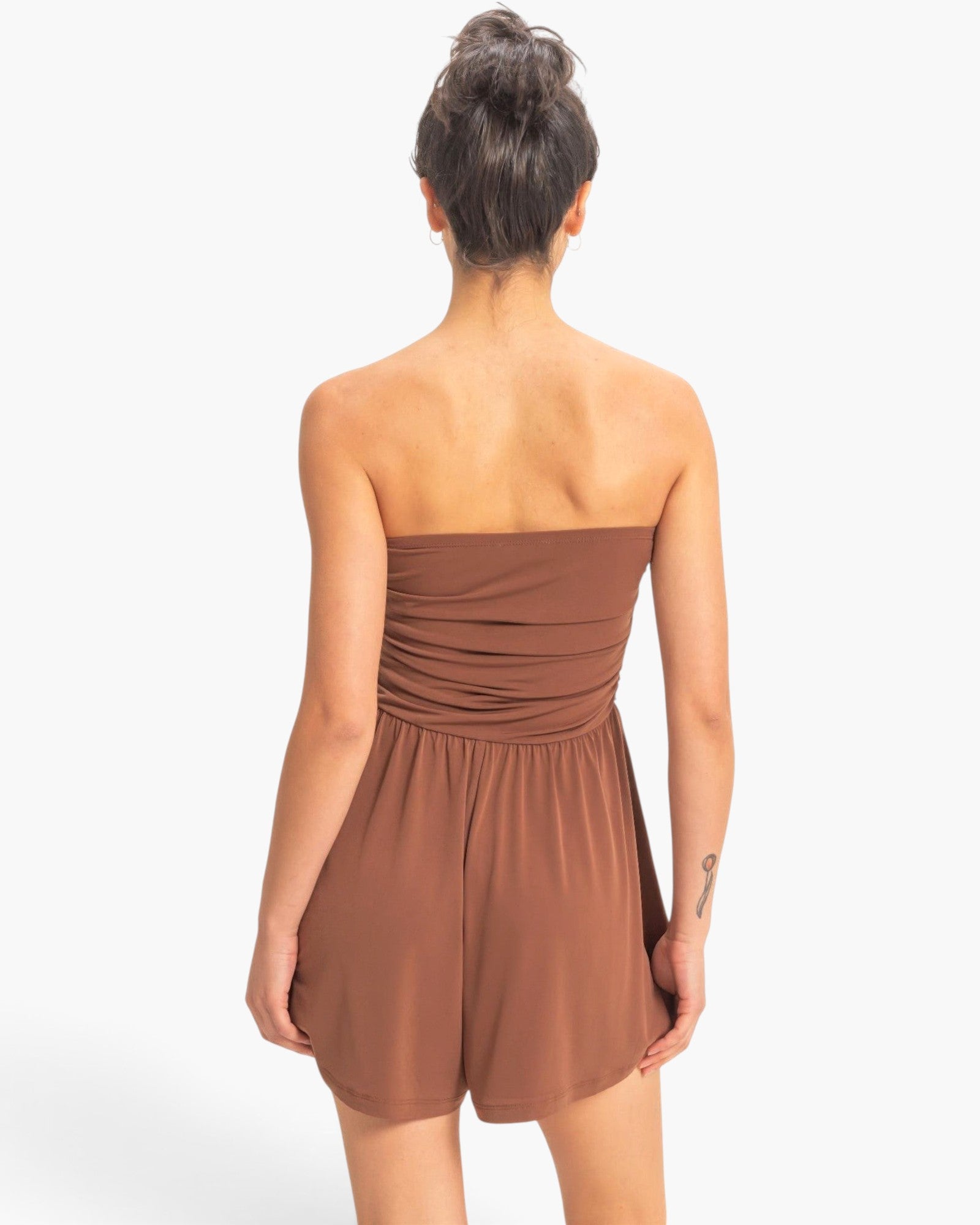Back view of a model wearing a brown Beach Rose Co. strapless romper with a shirred waist and relaxed shorts.
