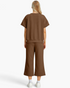 Back view of a woman wearing a Beach Rose Co. brown textured two-piece set with short sleeves and cropped pants.