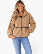 Beach Rose Co. camel sherpa jacket with black contrast trim, stand collar, and zip front worn by a smiling model.