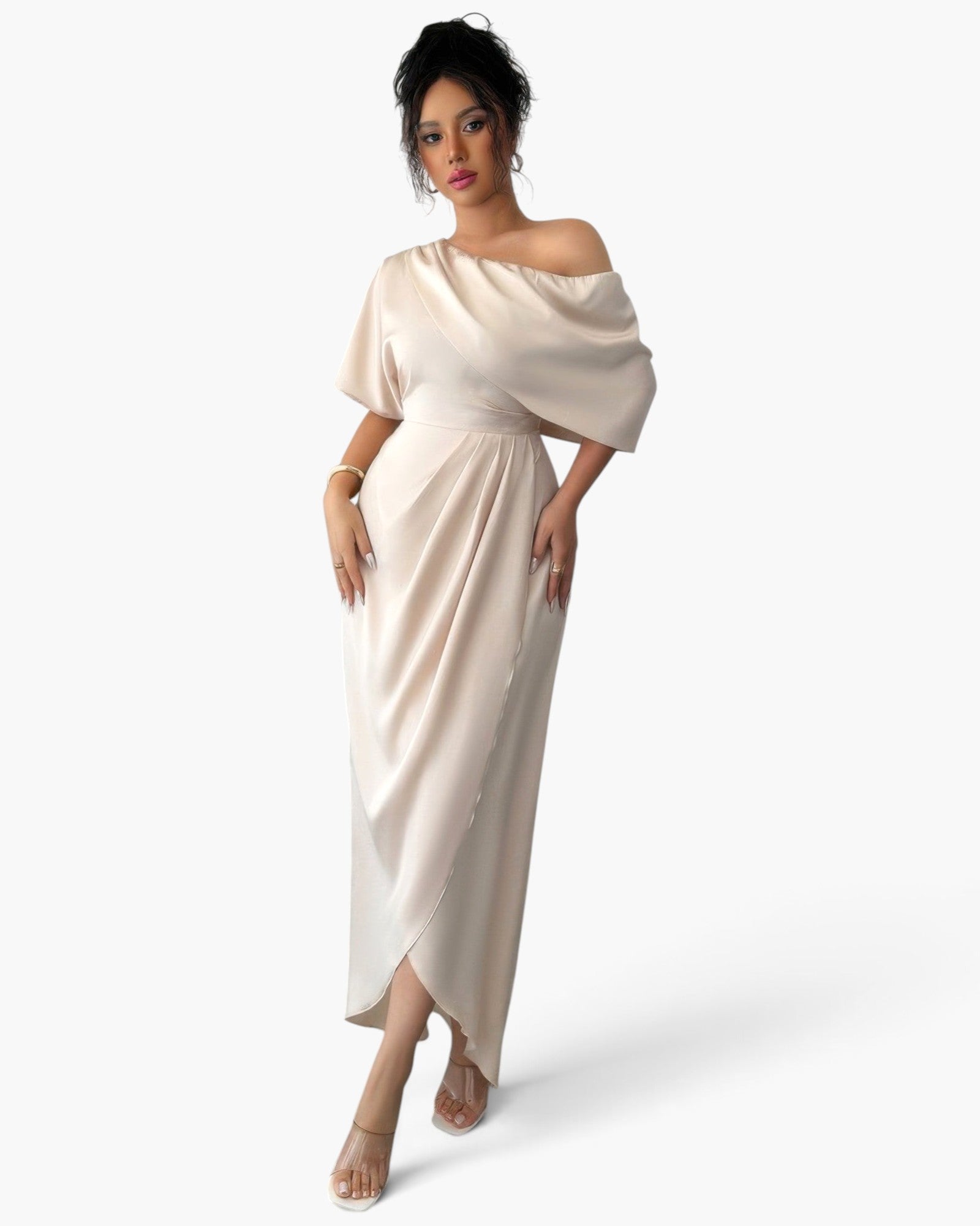 A woman modeling a floor-length off-the-shoulder dress in a light champagne beige satin fabric, set against a plain white studio background.