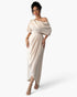 A woman modeling a floor-length off-the-shoulder dress in a light champagne beige satin fabric, set against a plain white studio background.