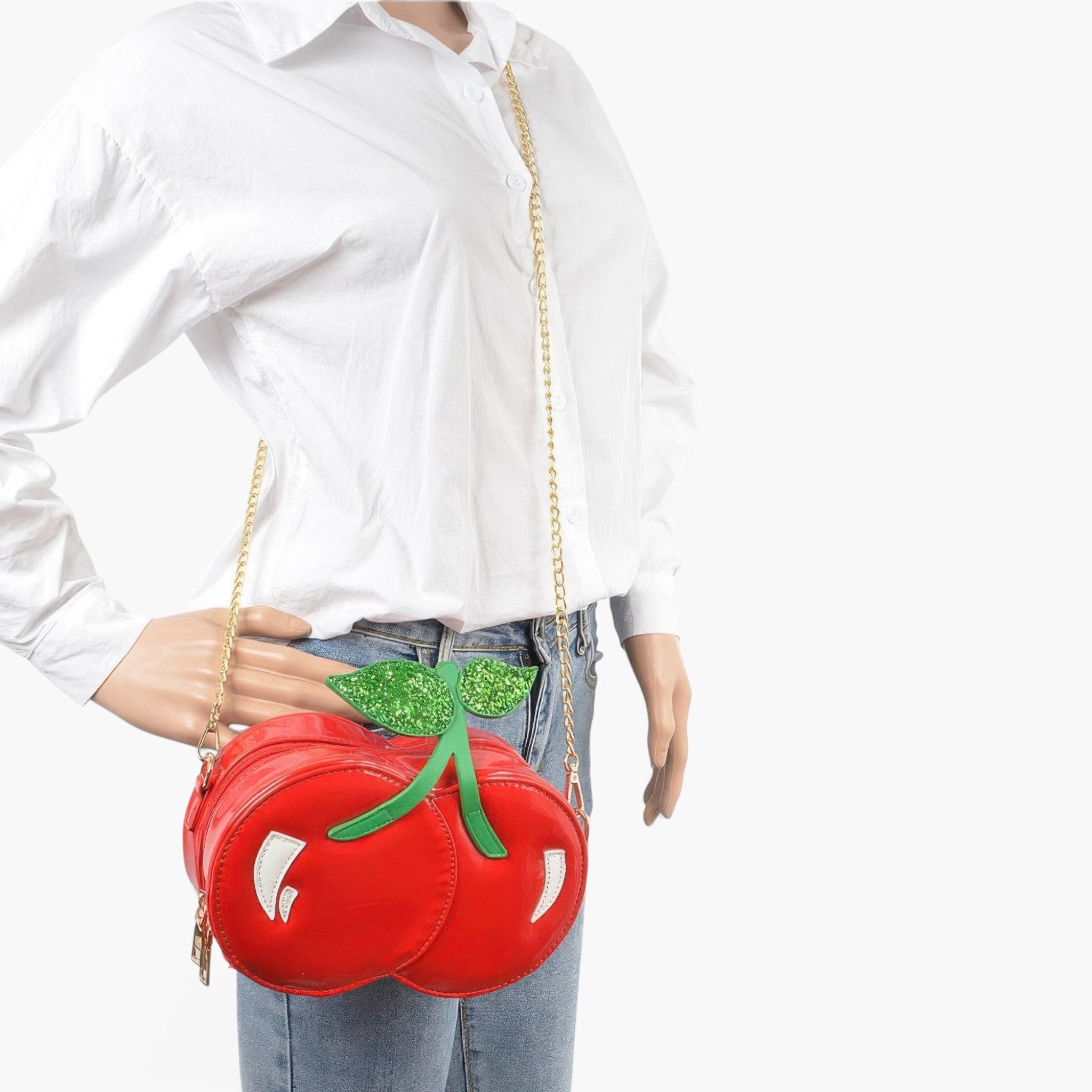 Beach Rose Co. red cherry-shaped clutch with glittery green leaves and a gold chain strap worn by a mannequin.