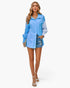 Beach Rose Co. light blue color block button down blouse with cuffed sleeves worn by a model with denim shorts.