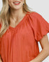 Beach Rose Co. coral orange puff sleeve blouse with gathered V-neck and textured fabric.
