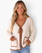 Beach Rose Co. cream knit cardigan with brown contrast trim, tie-front closure, and patch pockets on a smiling model.