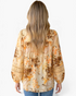 Beach Rose Co. cream blouse with floral and paisley print, long billowy sleeves, and lace inserts, back view.