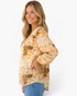 Beach Rose Co. cream floral and paisley blouse with billowy sleeves, lace inserts, and ladder trim on a model.