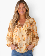 Beach Rose Co. cream floral and paisley blouse with billowy sleeves, lace inserts, and ladder trim on a smiling model.