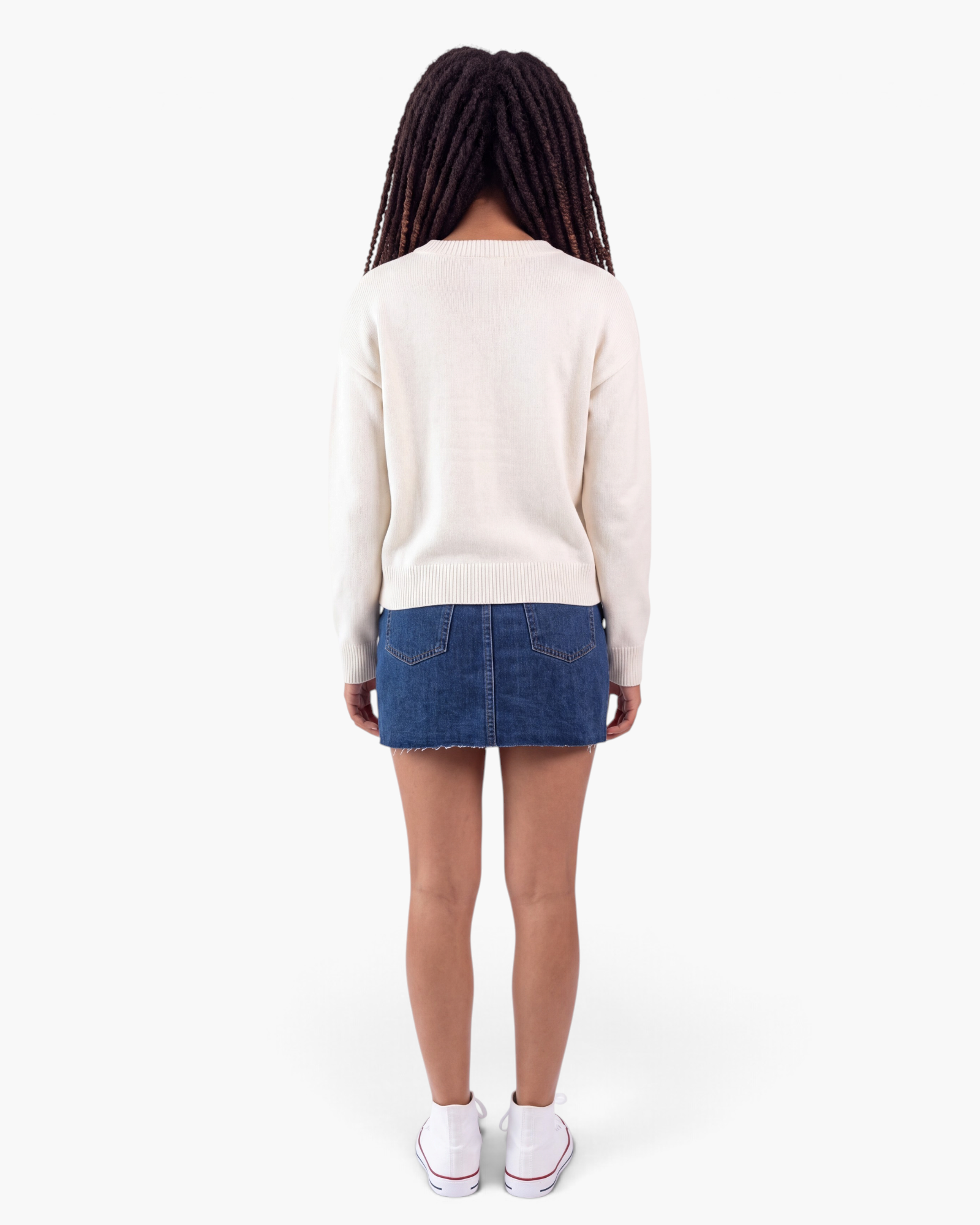 Beach Rose Co. cream knit sweater with ribbed trim worn from the back with a denim skirt and white sneakers.