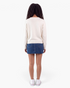Beach Rose Co. cream knit sweater with ribbed trim worn from the back with a denim skirt and white sneakers.