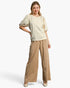 Beach Rose Co. cream knit top with puff sleeves and pearl embellishments worn by a smiling model with tan trousers