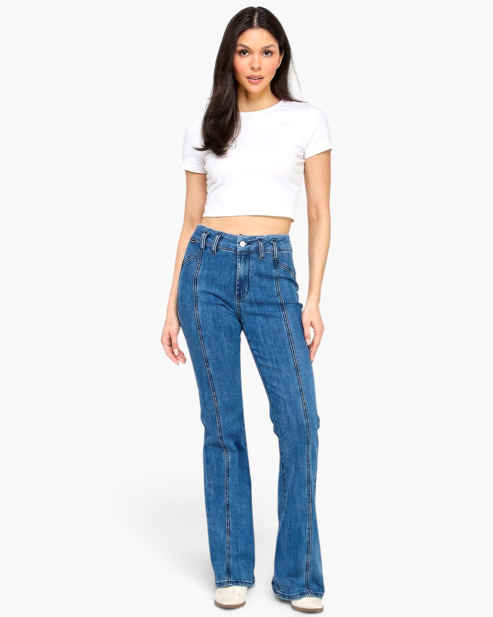 Model wearing Beach Rose Co. dark wash high-rise bell-bottom jeans with vertical seam detailing and a white crop top.