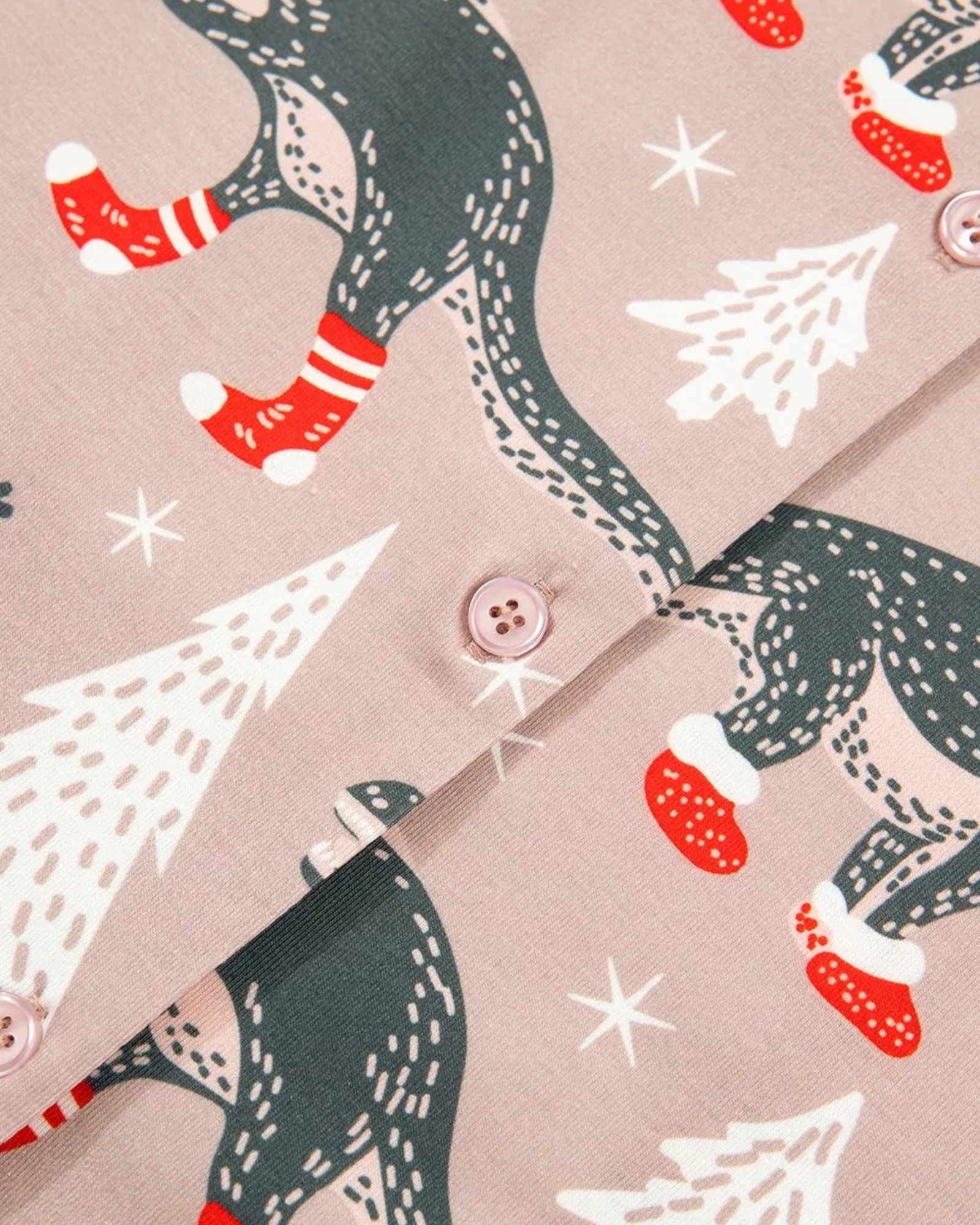 Beach Rose Co. taupe pajama set featuring charcoal dinosaurs in Santa hats and red booties with white Christmas trees.