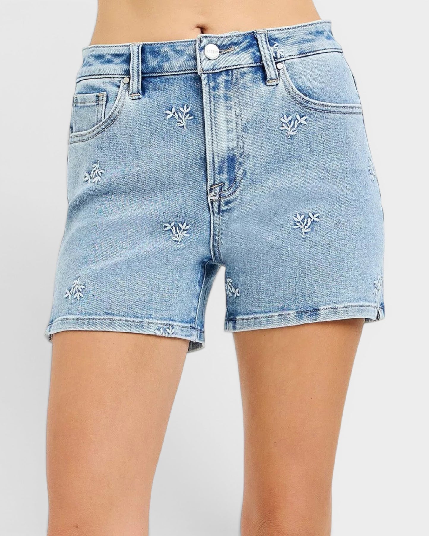 Beach Rose Co. light wash denim shorts with white embroidered floral details, high-rise, and short length.